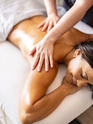 A person receives a soothing massage, relaxing with eyes closed, while a therapist gently works on their back.