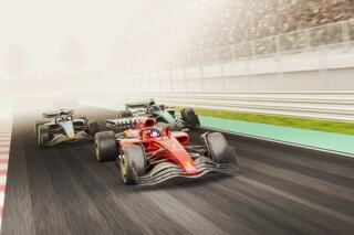 Two racing cars speed down a track, with one in a striking red and the other in green, amidst a foggy atmosphere and cheering spectators.