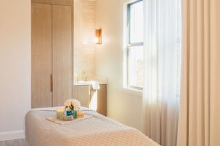 A serene spa room features a massage bed with decorative items, natural light, and a calming atmosphere enhanced by soft colors and textures.