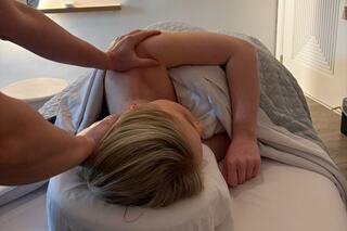 A person receives a massage while lying on a table, with a soothing atmosphere and a therapist gently working on their shoulders.
