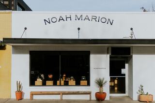A stylish storefront featuring "NOAH MARION" signage, with a bench and potted plants, showcasing a minimalist design and inviting ambiance.
