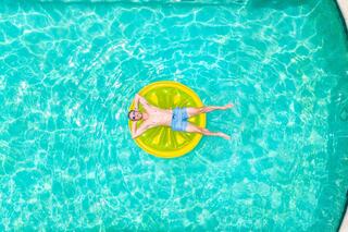 A person relaxes on a round, yellow float in clear blue water, enjoying a sunny day by the pool.