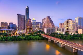 A vibrant city skyline at dusk, featuring modern skyscrapers reflecting in a river, with a bridge connecting both sides.