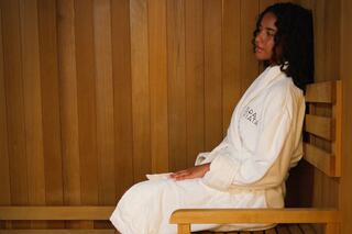 A person sits in a wooden sauna, dressed in a white robe, exuding a sense of calm and relaxation in the warm environment.
