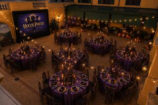 An enchanting outdoor setting with elegantly arranged purple tables, candles, and a "Hocus Pocus" movie screen, evoking a festive atmosphere.