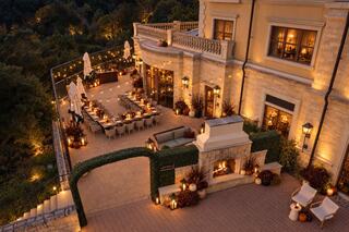 A beautifully lit outdoor dining area adorned with plants, cozy seating, and elegant decor, set against a nature backdrop.