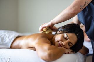 A woman relaxes on a massage table while receiving a soothing brush treatment, enjoying tranquility in a serene setting.