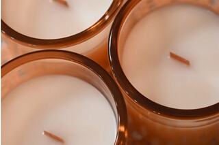 Four elegantly designed candles with white wax and wooden wicks, arranged closely in warm-toned holders. A cozy ambiance is evoked.