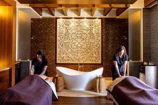 Two massage therapists work in a serene spa environment, featuring a stylish bathtub and an intricate decorative wall focal point.