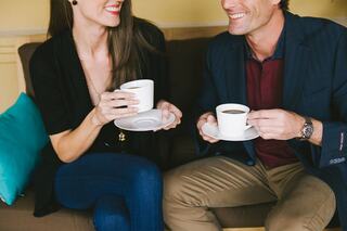 A couple enjoys coffee together, smiling and engaging in conversation, seated comfortably on a couch with a cozy ambiance.