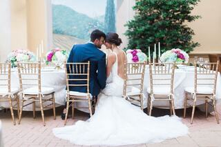 A couple sits closely at a beautifully set table adorned with floral arrangements and candles, enjoying an intimate moment together.