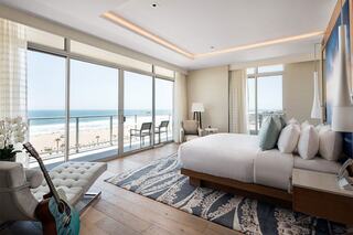 A modern beachfront hotel room with large windows, offering ocean views, plush bedding, and stylish decor, creating a serene atmosphere.