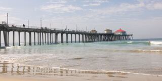 A bustling pier stretches over calm waves, with people strolling and enjoying the ocean view under a partly cloudy sky.