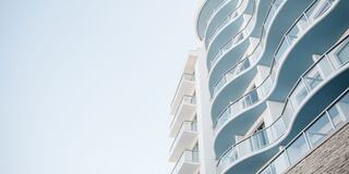 A modern building with a curvy facade features multiple balconies and a light, airy design against a clear sky backdrop.
