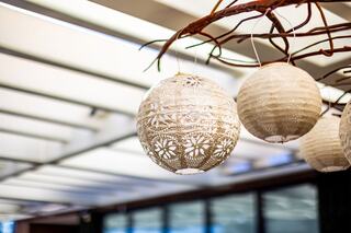 Delicate paper lanterns hang from a branch, softly illuminated against a modern, airy backdrop with subtle lines and natural elements.