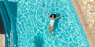 A person relaxes in a clear blue pool, floating on their back amidst shimmering water, exuding tranquility and leisure.