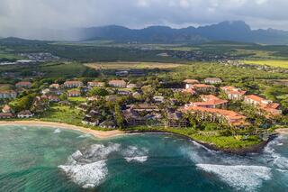 A coastal resort features lush greenery, sandy beaches, and waves crashing against the shore, set against a backdrop of rolling hills.