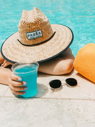 A relaxing scene by the pool with a straw hat, a blue drink, a cozy orange towel, and stylish sunglasses. Perfect for a sunny day!