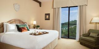 A cozy, well-furnished hotel room with a large bed, comfortable chair, and a beautiful view through sliding glass doors.