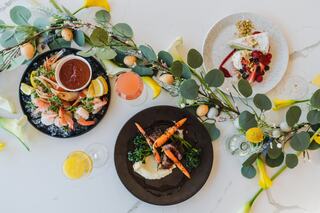 A colorful spread of seafood, grilled meat, and dessert, adorned with fresh flowers and greenery, all arranged elegantly on a table.