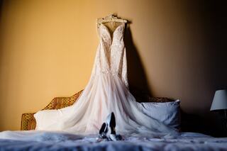 A delicate wedding dress hangs gracefully above a bed, accompanied by elegant shoes, creating a romantic and inviting atmosphere.