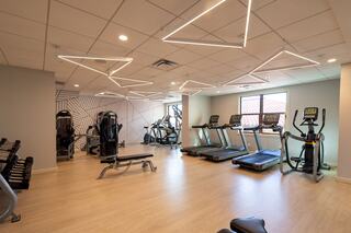 A modern gym features sleek equipment, including treadmills and weight machines, highlighted by stylish LED ceiling lights and a bright atmosphere.