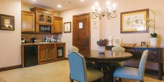 A cozy dining area features a round table, stylish chairs, and a kitchenette with wooden cabinetry, creating a warm and inviting atmosphere.