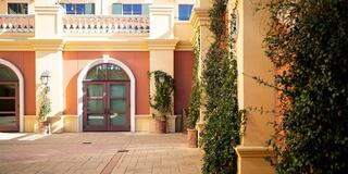 A warm, inviting courtyard features an arched doorway, lush greenery, and elegant architectural details, creating a peaceful atmosphere.
