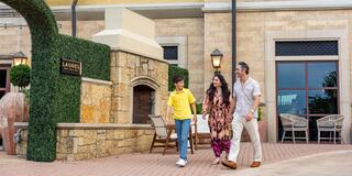 A family joyfully walks along a stylish outdoor area, surrounded by greenery and elegant architecture, enjoying their time together.