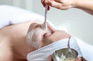 A person receives a facial treatment with a gentle application of cream using a brush, creating a soothing spa atmosphere.