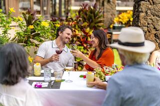 A couple shares a joyful toast at a lively outdoor gathering, surrounded by greenery and colorful flowers, creating a warm, festive atmosphere.