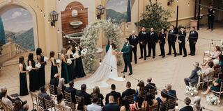 A couple exchanges vows in a beautiful outdoor ceremony. Guests sit in rows, surrounded by elegant decor and a floral arch.