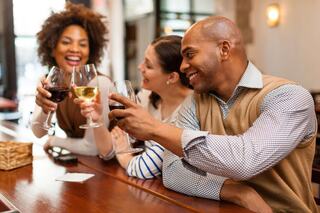 Three friends enjoy drinks at a bar, laughing and toasting together, creating a joyful and relaxed atmosphere.