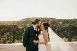 A couple shares a romantic kiss during sunset, surrounded by lush green hills, capturing a heartfelt wedding moment.