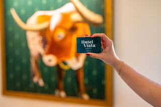A hand holds a hotel key card with a colorful longhorn painting in the background, showcasing a vibrant and artistic atmosphere.