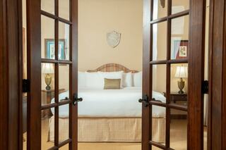 A cozy, elegantly furnished bedroom with a large bed, decorative elements, and warm lighting, framed by double doors.