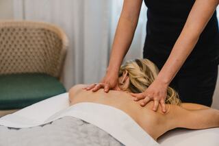 A person receives a massage, lying face down on a table, while a therapist applies soothing pressure to their back. Relaxing ambiance evident.