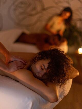 A serene spa setting features a person receiving a massage, while another therapist is visible in the background, creating a tranquil atmosphere.