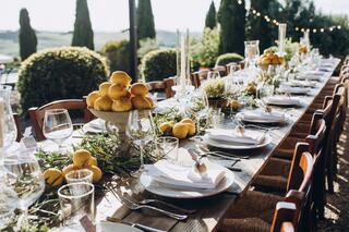 A beautifully set outdoor dining table adorned with fresh lemons, greenery, elegant glassware, and candles, surrounded by a scenic landscape.