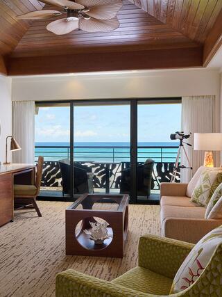 Spacious room with beach views, wooden ceiling, modern decor, and a cozy seating area. A telescope overlooks the ocean, inviting relaxation.