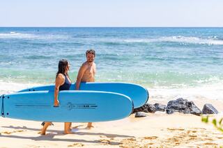 A man and woman walk along a sandy beach, carrying vibrant blue surfboards, with the ocean waves gently lapping in the background.