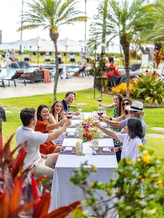 A cheerful group celebrates together outdoors at a beautifully arranged table, raising glasses amidst lush greenery and vibrant flowers.