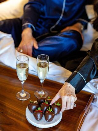 A cozy setting features two glasses of champagne and a plate of chocolate-covered strawberries, creating an intimate moment.