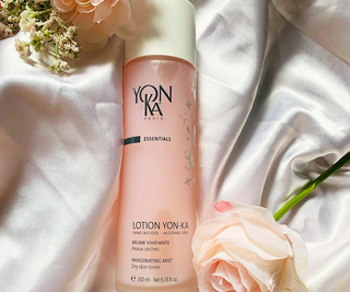 A pink toner bottle on soft fabric, accompanied by delicate flowers, conveys a sense of elegance and refreshing skincare.