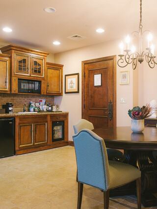 A cozy kitchen features wooden cabinetry, a round dining table with chic chairs, and warm lighting, creating an inviting atmosphere.