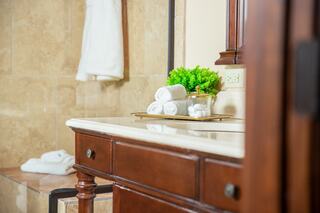 A well-lit bathroom features a wooden vanity with rolled towels and a small plant, complemented by stone walls and plush towels hanging nearby.