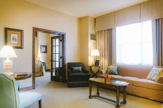 A cozy living area featuring a sofa, armchair, lamps, and a wooden table, with warm lighting and soft decor, creating an inviting atmosphere.