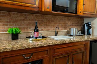 A cozy kitchen features wooden cabinets, a granite countertop, a wine bottle on a tray, and a coffee maker alongside a small sink.