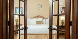 A cozy bedroom awaits, featuring a large bed, soft linens, bedside lamps, and warm decor viewed through double doors.