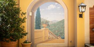 A beautifully painted mural simulates a balcony view of rolling hills, framed by a potted plant and warm, inviting colors.